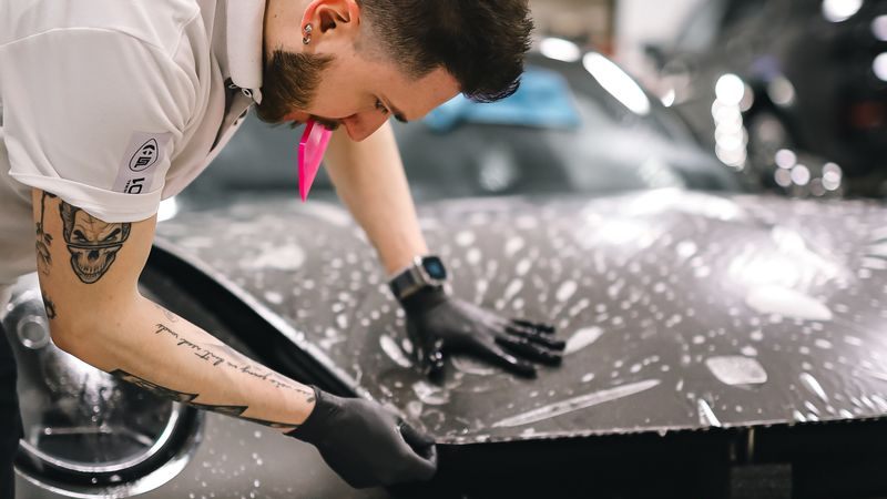 Technician applying paint protection film to a car hood